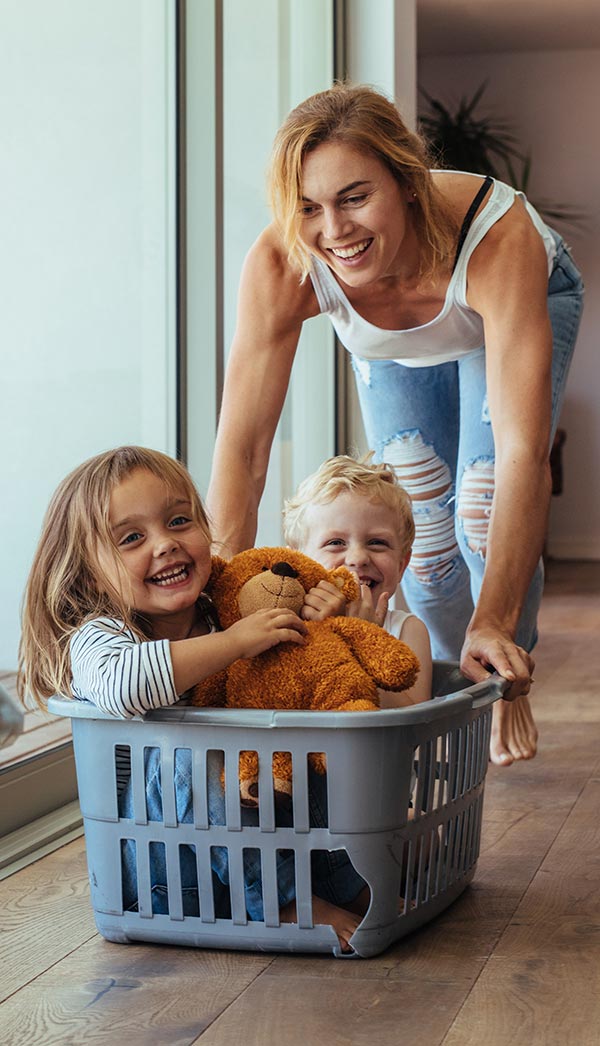 Two children playing with a teddy bear in a laundry basket.